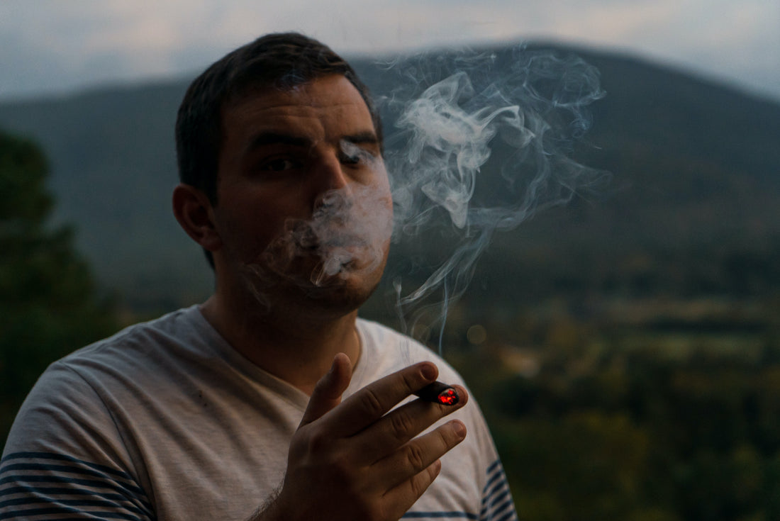 Man smoking ina field with mountains in the background 